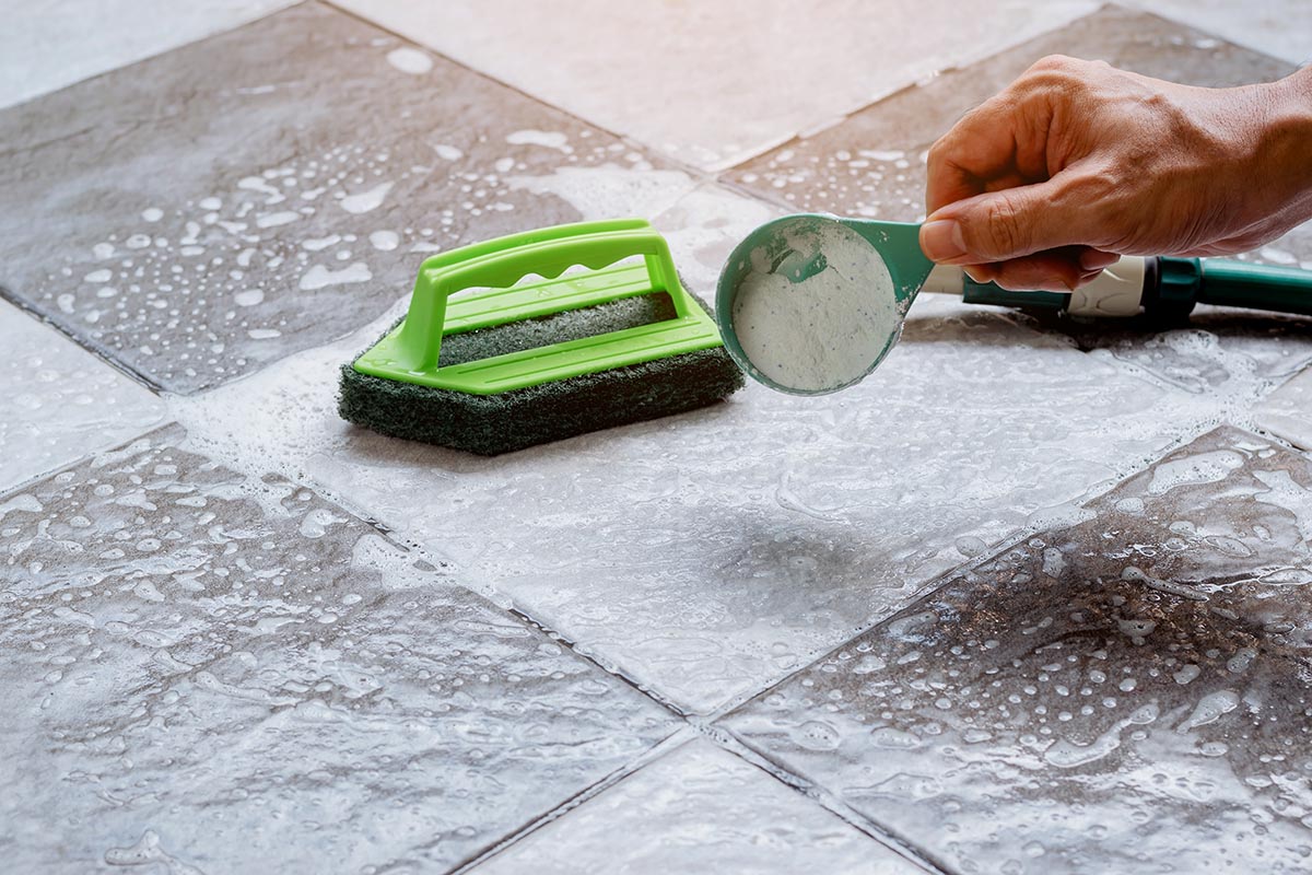 man poring detergent on wet bathoorm floor tiles before cleaning